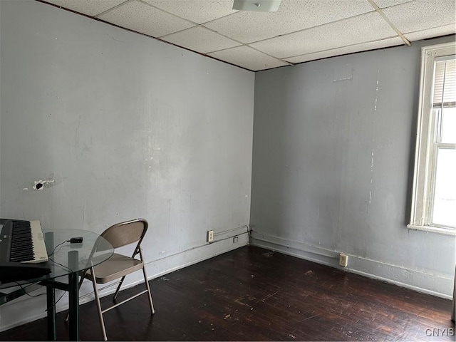 unfurnished office featuring a wealth of natural light, a paneled ceiling, baseboards, and wood finished floors