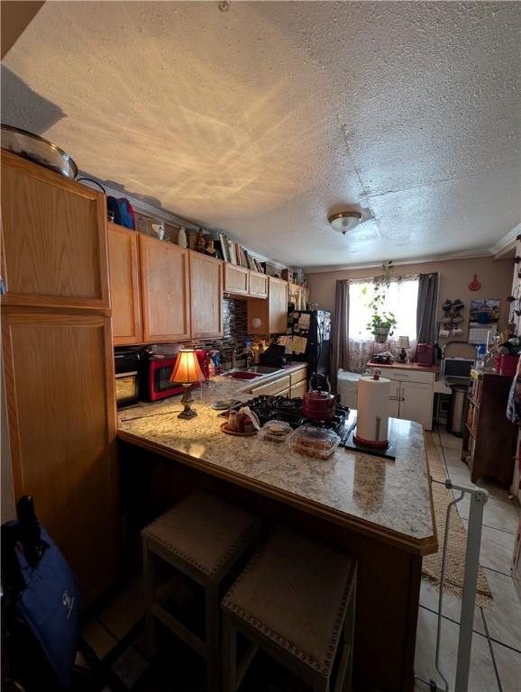 kitchen with light tile patterned floors, light countertops, a textured ceiling, a peninsula, and a kitchen bar