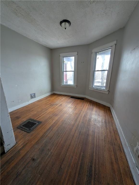 spare room featuring wood-type flooring, visible vents, baseboards, and a textured ceiling