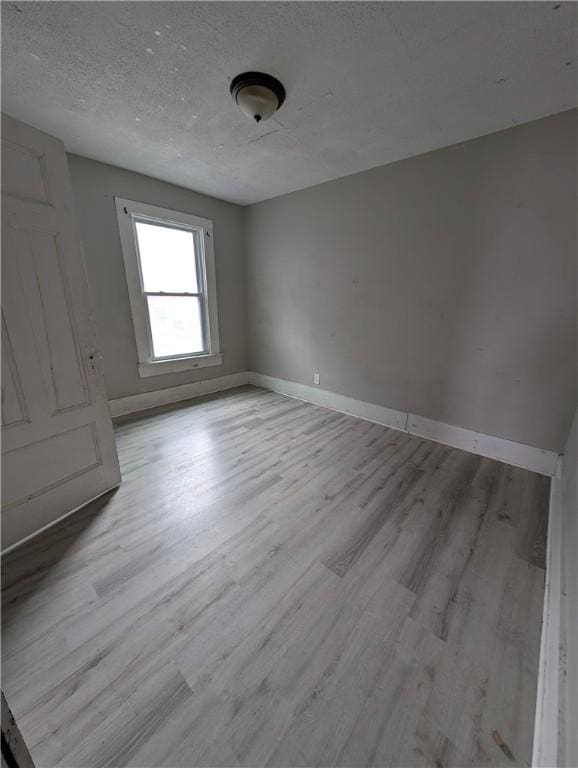 unfurnished room featuring a textured ceiling, light wood-style flooring, and baseboards