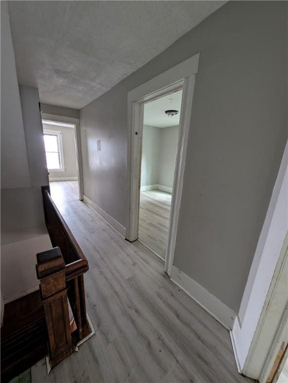 corridor featuring a textured ceiling, baseboards, wood finished floors, and an upstairs landing