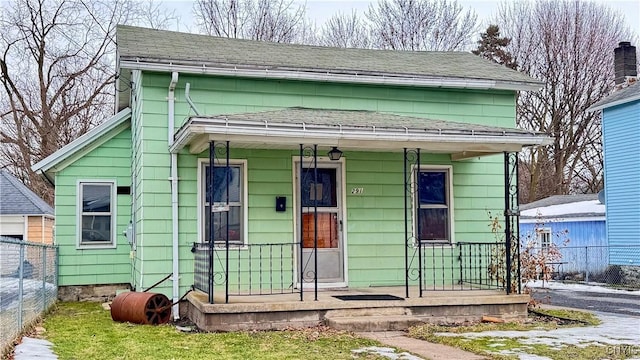 view of front facade featuring covered porch, fence, and roof with shingles