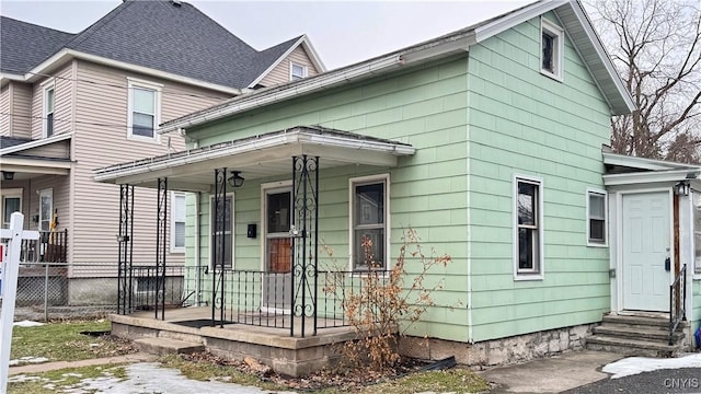 view of front of home with entry steps, covered porch, fence, and roof with shingles