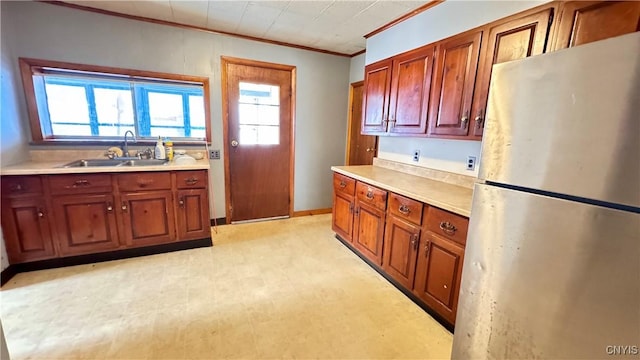 kitchen featuring light floors, light countertops, ornamental molding, freestanding refrigerator, and a sink