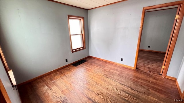 empty room featuring ornamental molding, hardwood / wood-style floors, visible vents, and baseboards