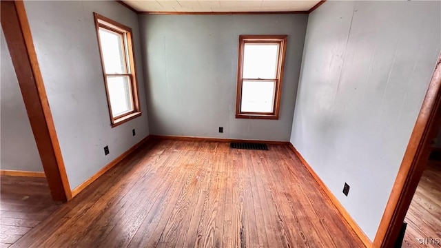 unfurnished room featuring hardwood / wood-style flooring, visible vents, and baseboards