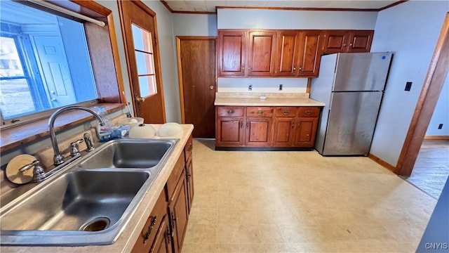 kitchen featuring a sink, light countertops, ornamental molding, freestanding refrigerator, and light floors