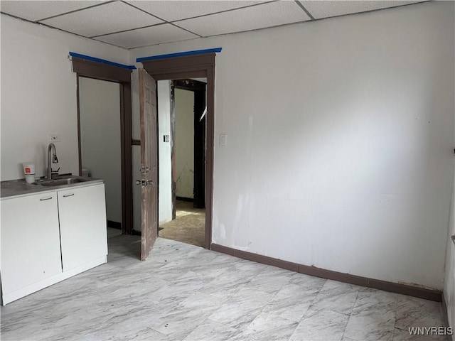 spare room with a drop ceiling, a sink, and baseboards