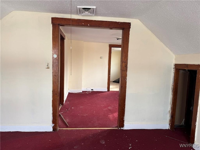 hallway featuring a textured ceiling, carpet, lofted ceiling, and visible vents