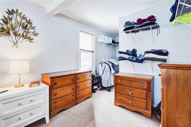 walk in closet featuring light colored carpet and beamed ceiling