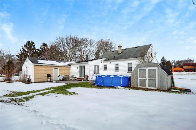 snow covered property featuring a shed, an outdoor pool, and an outdoor structure