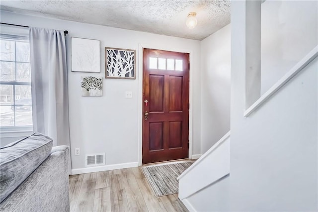 entrance foyer with light wood finished floors, a textured ceiling, visible vents, and a wealth of natural light