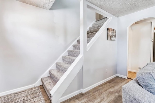 stairs with arched walkways, a textured ceiling, wood finished floors, and baseboards