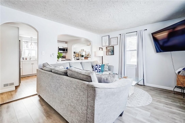 living room featuring visible vents, light wood-style flooring, and a textured ceiling