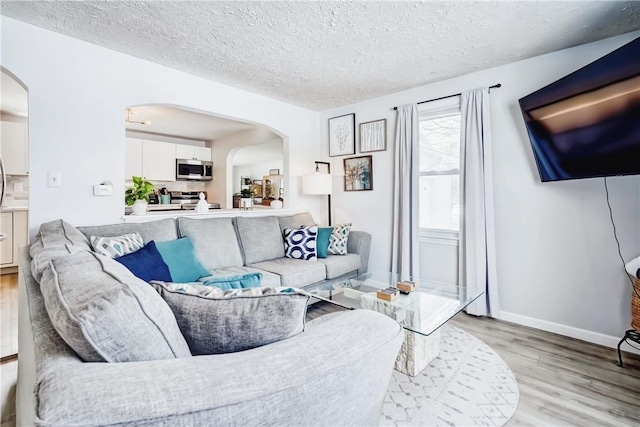 living area with arched walkways, a textured ceiling, baseboards, and light wood-style floors