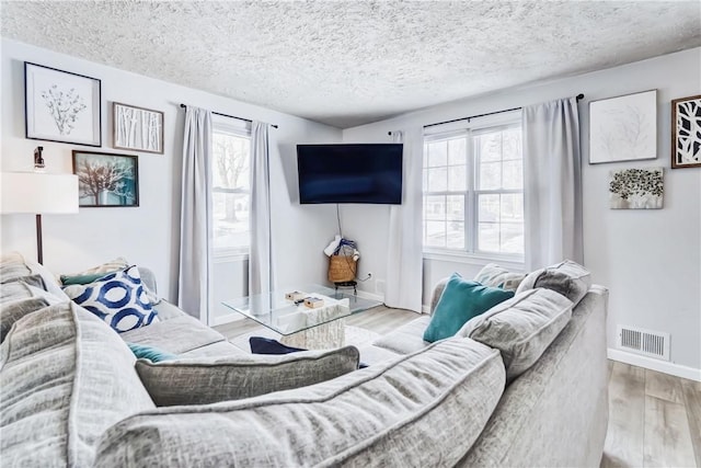 living room with a textured ceiling, wood finished floors, visible vents, and baseboards