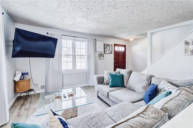 living room with baseboards, a textured ceiling, visible vents, and wood finished floors