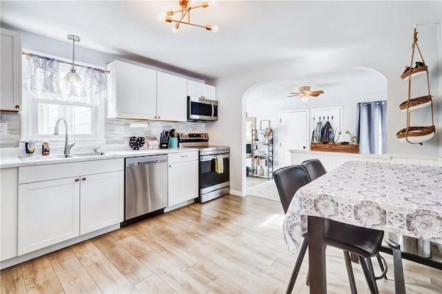 kitchen featuring arched walkways, appliances with stainless steel finishes, a sink, light wood-style floors, and backsplash