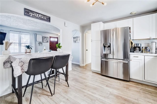 kitchen featuring arched walkways, light wood finished floors, light countertops, white cabinetry, and stainless steel fridge with ice dispenser