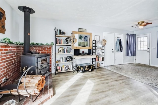 interior space with a ceiling fan, a wood stove, and wood finished floors