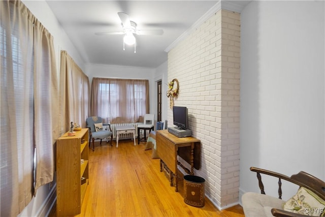 living area with light wood finished floors, brick wall, ornamental molding, and a ceiling fan