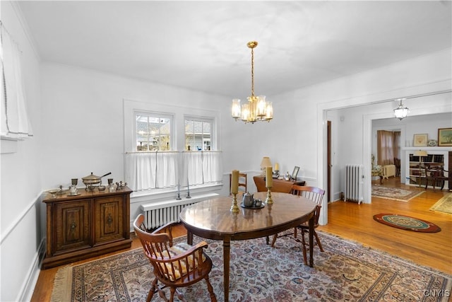 dining area with radiator, baseboards, a chandelier, and wood finished floors