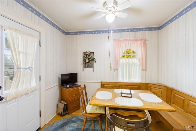 dining space with wood finished floors, ceiling fan, and wallpapered walls