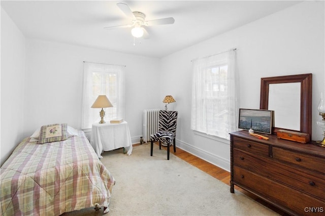 bedroom featuring ceiling fan, radiator, multiple windows, and baseboards