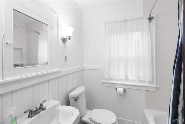 bathroom featuring curtained shower, wainscoting, toilet, and a tub