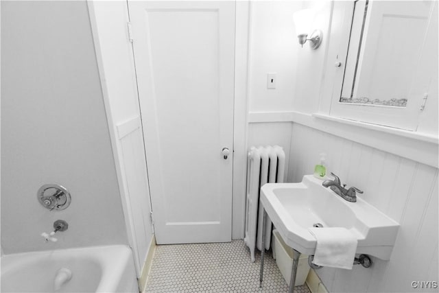 bathroom with a wainscoted wall, radiator heating unit, tub / shower combination, and a sink