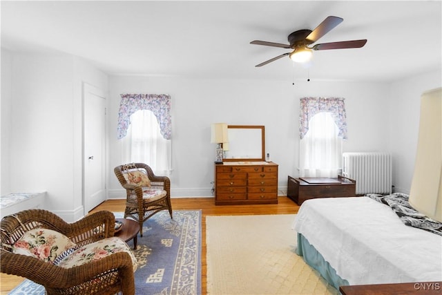 bedroom featuring radiator, multiple windows, baseboards, and light wood finished floors