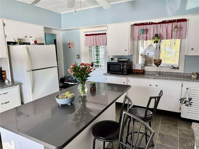 kitchen with freestanding refrigerator, black microwave, white cabinetry, and dark countertops