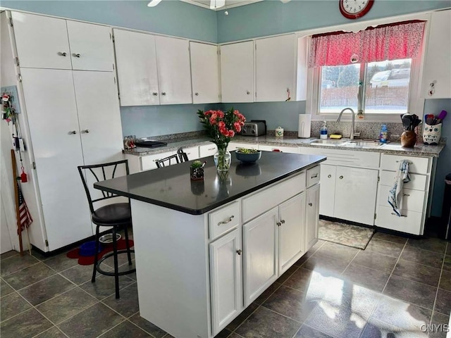 kitchen featuring a kitchen island, white cabinets, a sink, and a breakfast bar area