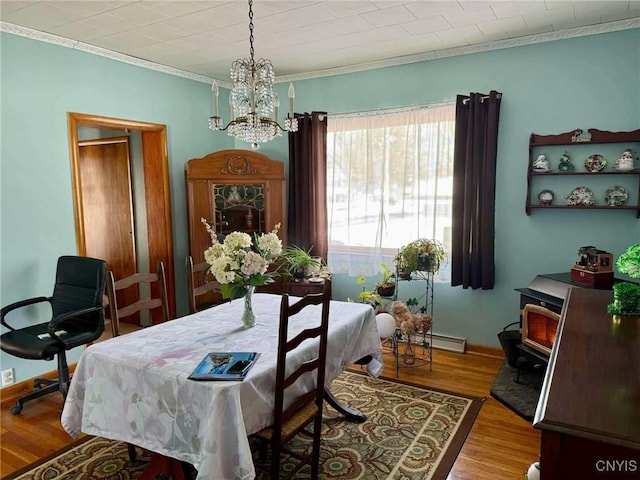 dining space featuring crown molding, wood finished floors, a wood stove, and a notable chandelier