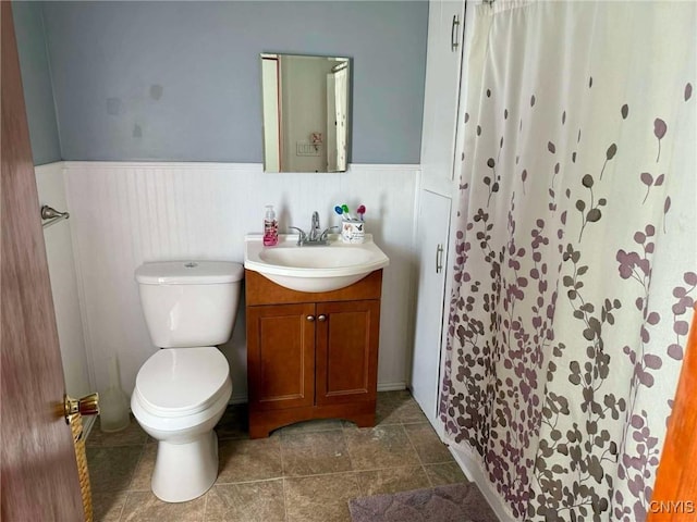 bathroom featuring curtained shower, wainscoting, vanity, and toilet