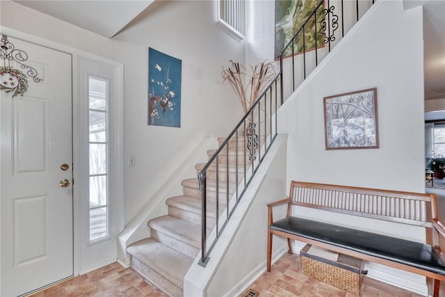 entryway with brick floor, a towering ceiling, stairway, and baseboards