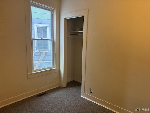 unfurnished bedroom featuring a closet, visible vents, dark carpet, and baseboards