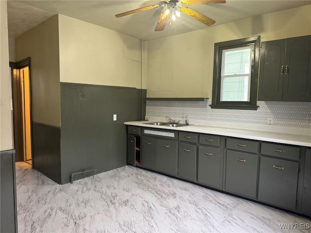 kitchen with a sink, a ceiling fan, marble finish floor, light countertops, and wainscoting