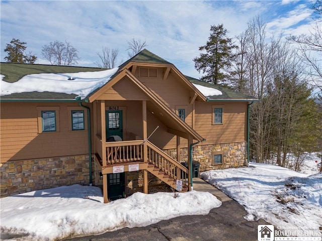 snow covered property with stone siding and stairway