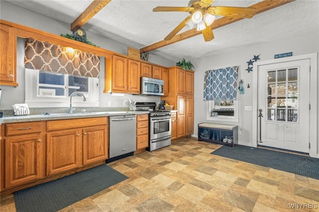 kitchen featuring a textured ceiling, stainless steel appliances, a sink, light countertops, and brown cabinets