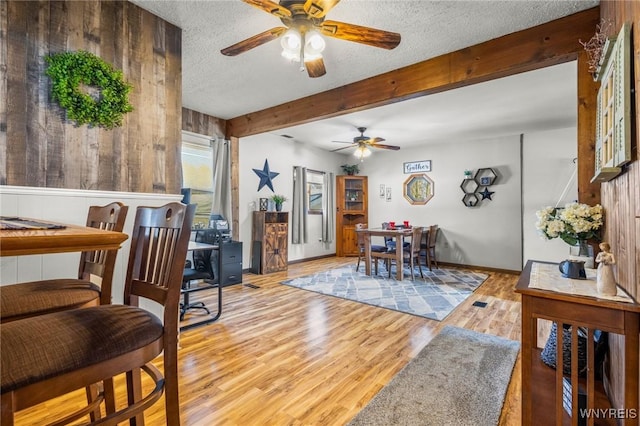 dining room with baseboards, ceiling fan, beamed ceiling, wood finished floors, and a textured ceiling