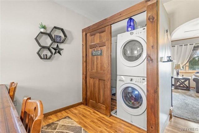 clothes washing area with laundry area, baseboards, light wood finished floors, and stacked washer / dryer