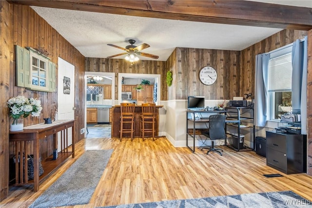 home office with wooden walls, light wood-type flooring, beamed ceiling, and a textured ceiling