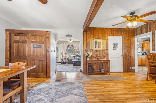 foyer entrance with light wood-style flooring, arched walkways, ceiling fan, and wooden walls