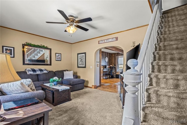 carpeted living room with arched walkways, stairway, ornamental molding, ceiling fan, and baseboards