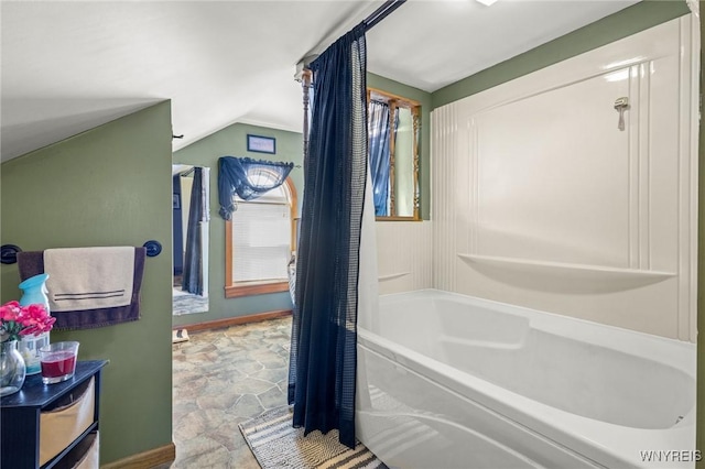 bathroom with vaulted ceiling, stone finish flooring, shower / bath combo, and baseboards