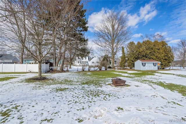 yard covered in snow featuring an outdoor fire pit, fence, a residential view, and an outbuilding