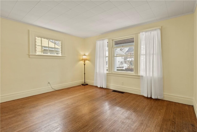 unfurnished room with a healthy amount of sunlight, baseboards, visible vents, and wood finished floors