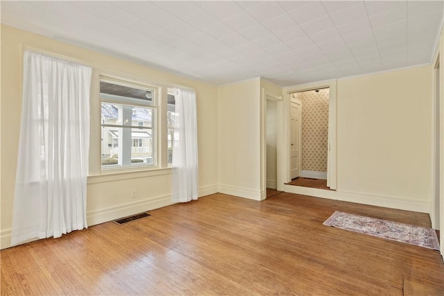 empty room featuring baseboards, visible vents, wood finished floors, and ornamental molding