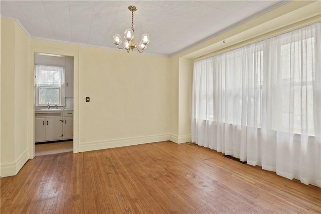 unfurnished room featuring crown molding, an inviting chandelier, a sink, light wood-type flooring, and baseboards